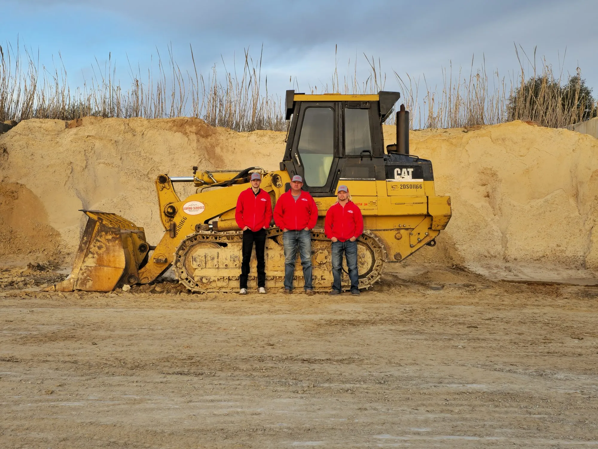 Three Ledford Services crew members in front of a CAT track loader at a dirt job