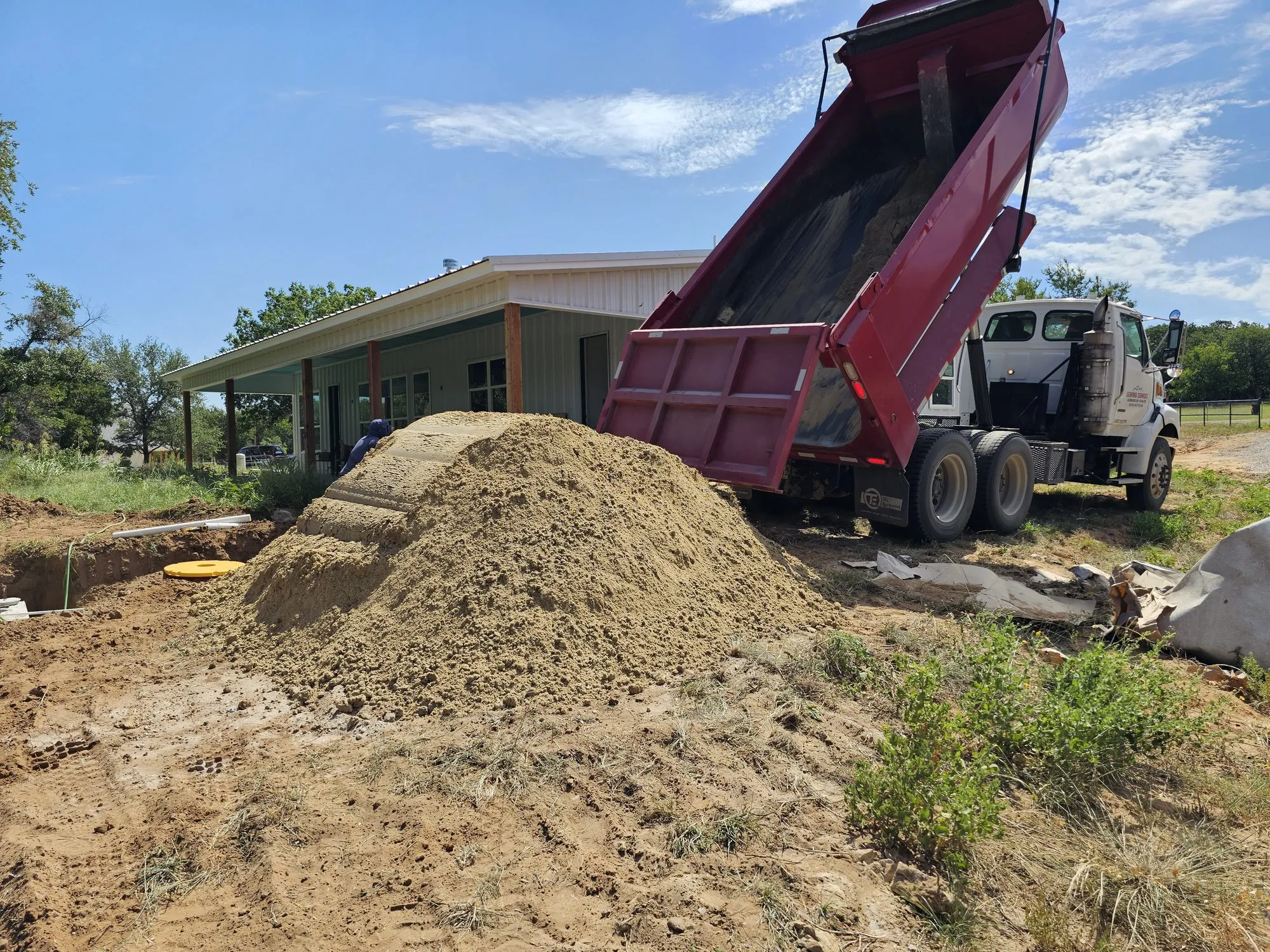 A Ledford Services dump truck tipping a load of fill beside a house