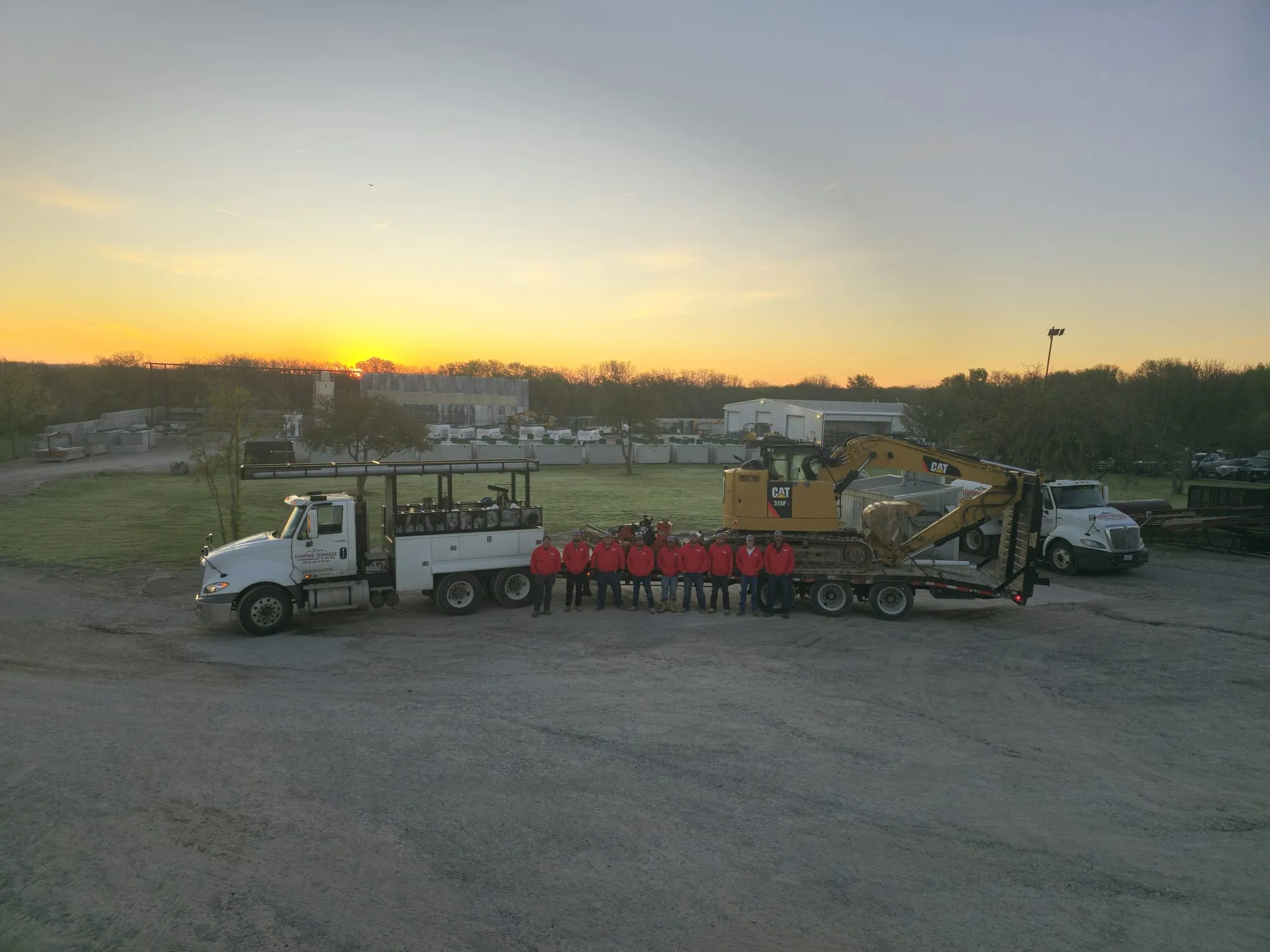 Ledford Services trucks and a CAT excavator staged at a job site at sunrise